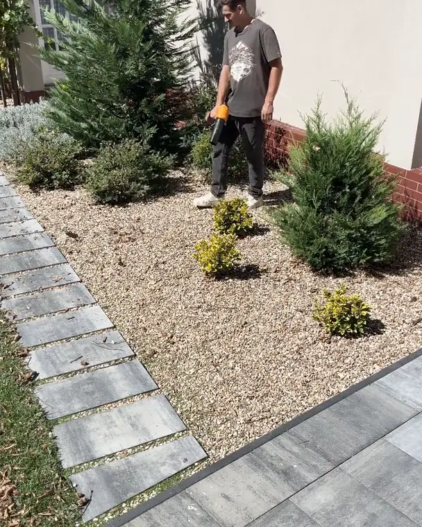 The same garden bed and paths clear of leaves, with the tester holding the SuperLeafBlower