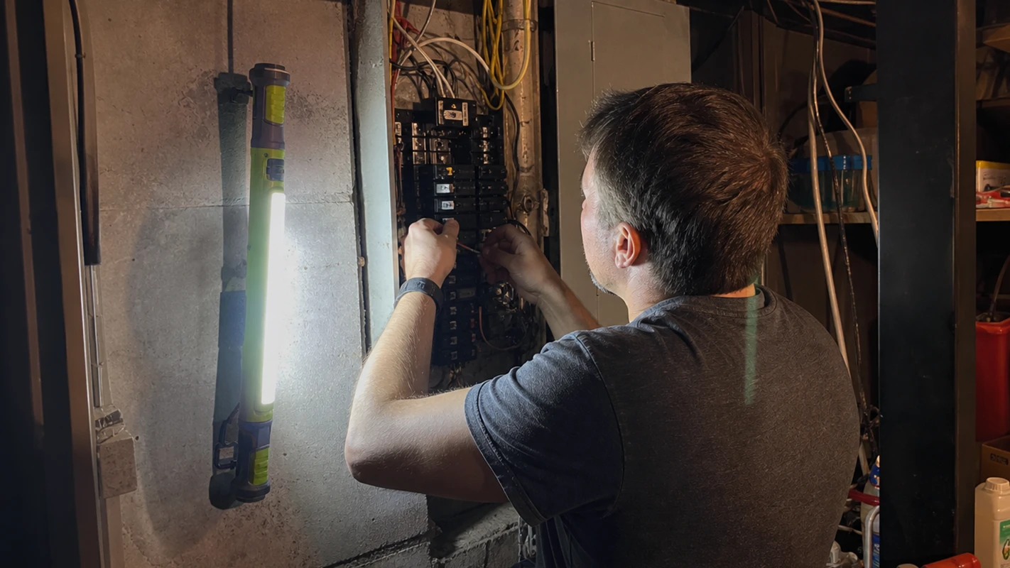 SuperTorch magnetically stuck to the wall beside a breaker panel while a homeowner traces a circuit hands-free