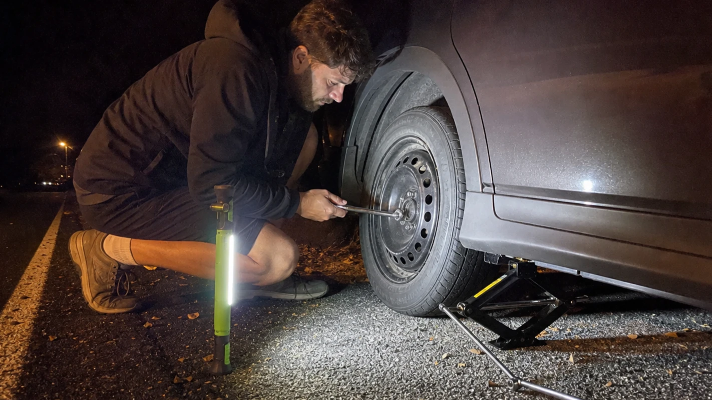 SuperTorch standing beside a driver changing a flat tire on the shoulder at night